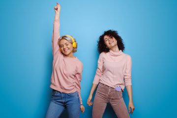 Caucasian women listening to music and dance on a blue studio wall wearing headphones